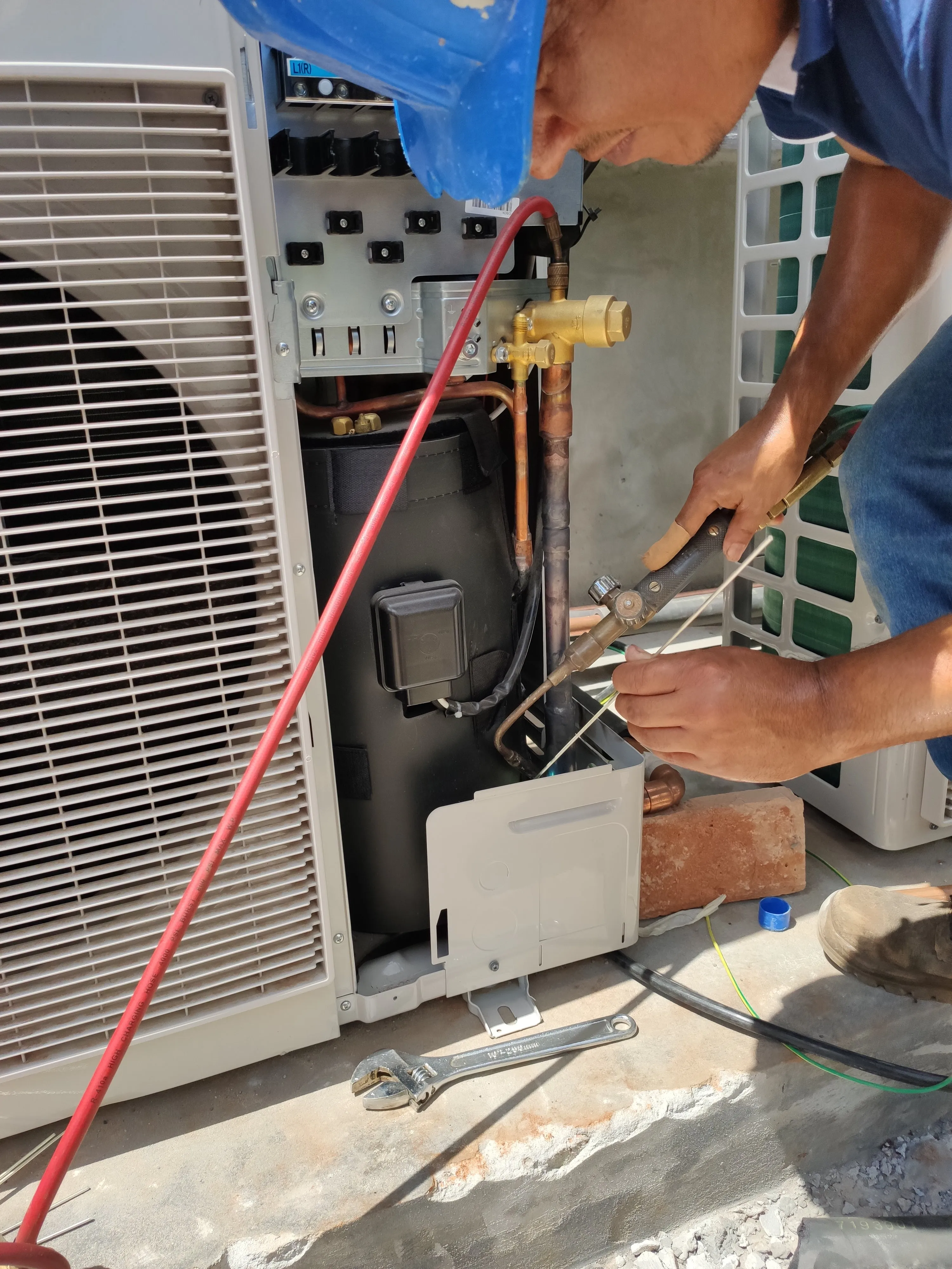 Técnico ajustando las conexiones de una unidad exterior de aire acondicionado.